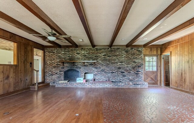 867 Lexington Hwy, Loretto, TN 38469 - unfurnished living room with wooden walls, beamed ceiling, ceiling fan, a fireplace, and brick wall