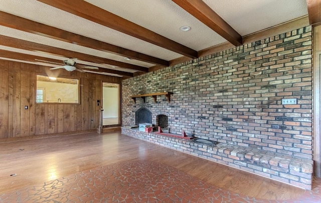 867 Lexington Hwy, Loretto, TN 38469 - unfurnished living room featuring beam ceiling, a brick fireplace, ceiling fan, wooden walls, and wood finished floors