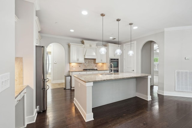 1000 Swanson Ln, Franklin, TN 37064 - kitchen featuring arched walkways, appliances with stainless steel finishes, crown molding, a center island with sink, and dark wood-style floors