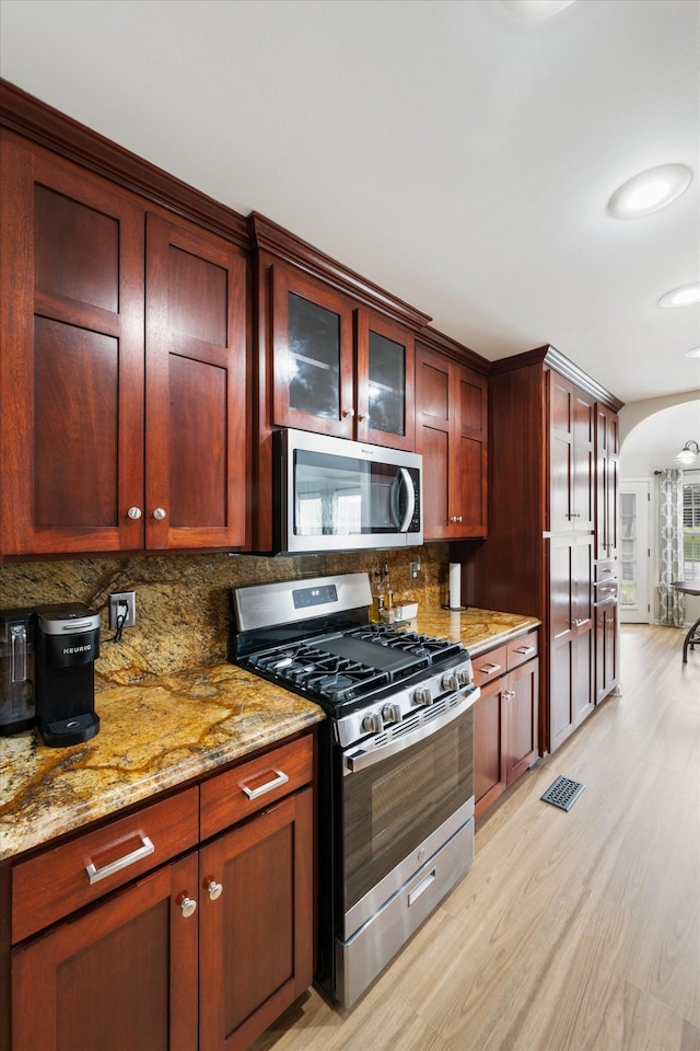 305 Davis Green Ln, Spring Hill, TN 37174 - kitchen with stainless steel appliances, arched walkways, light wood-type flooring, tasteful backsplash, and light stone countertops