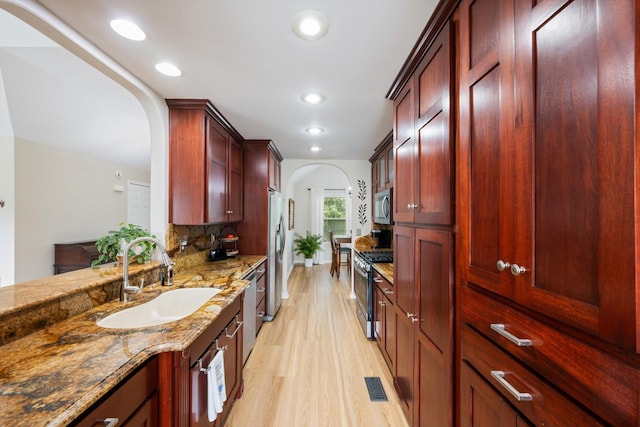 305 Davis Green Ln, Spring Hill, TN 37174 - kitchen with arched walkways, appliances with stainless steel finishes, reddish brown cabinets, light stone counters, and light wood finished floors