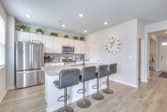 207 Welara St, Murfreesboro, TN 37129 - kitchen with appliances with stainless steel finishes, a center island with sink, light wood-style floors, tasteful backsplash, and recessed lighting