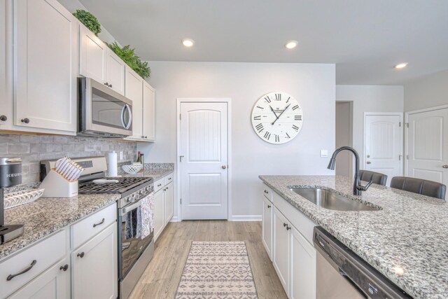 207 Welara St, Murfreesboro, TN 37129 - kitchen with appliances with stainless steel finishes, light wood finished floors, decorative backsplash, light stone countertops, and white cabinetry