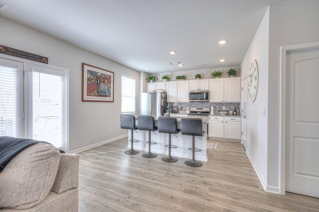207 Welara St, Murfreesboro, TN 37129 - kitchen featuring stainless steel appliances, a kitchen bar, decorative backsplash, white cabinets, and light wood-style floors