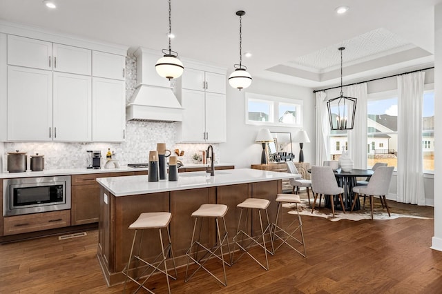 7405 Leelee Dr, Franklin, TN 37064 - kitchen with stainless steel microwave, a tray ceiling, premium range hood, light countertops, and backsplash