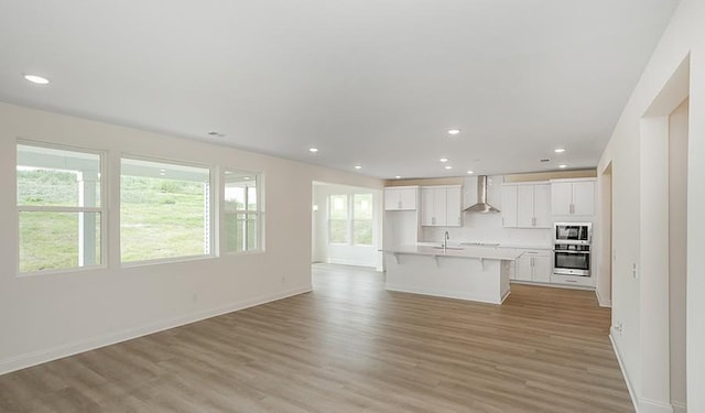 2901 Windstone Trl, Columbia, TN 38401 - kitchen featuring stainless steel appliances, wall chimney range hood, white cabinets, open floor plan, and a kitchen breakfast bar