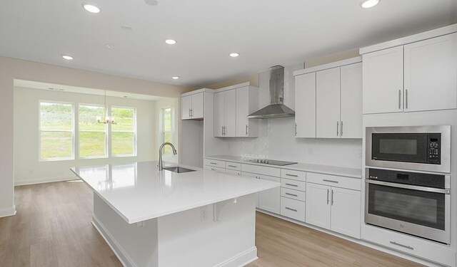 2901 Windstone Trl, Columbia, TN 38401 - kitchen with appliances with stainless steel finishes, wall chimney range hood, light wood-style floors, light countertops, and a kitchen island with sink