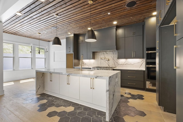 1884 Barnstaple Ln, Brentwood, TN 37027 - kitchen featuring light stone countertops, tasteful backsplash, an island with sink, custom range hood, and hanging light fixtures