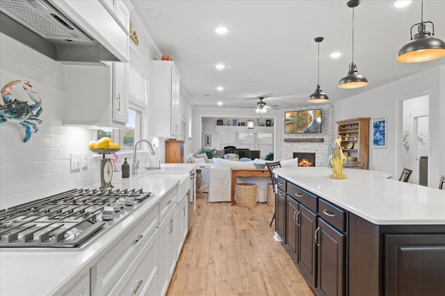 1055 Sumner Grv, Spring Hill, TN 37174 - kitchen featuring exhaust hood, stainless steel gas cooktop, a stone fireplace, a ceiling fan, and white cabinetry