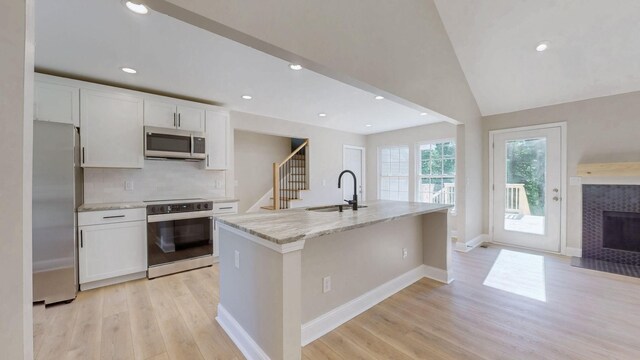 7313 Horn Tavern Ct, Fairview, TN 37062 - kitchen featuring stainless steel appliances, light wood-style floors, white cabinetry, light stone countertops, and a center island with sink