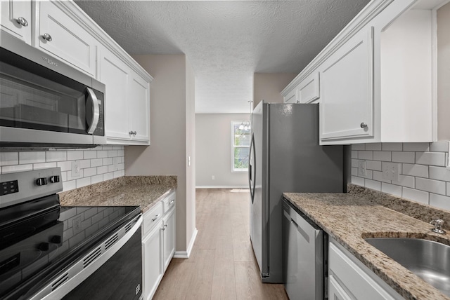 3798 Bret Dr, Clarksville, TN 37040 - kitchen featuring appliances with stainless steel finishes, white cabinets, light wood-style floors, decorative backsplash, and a textured ceiling