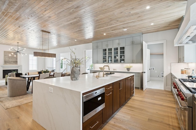 6315 Callie Ln, Brentwood, TN 37027 - kitchen with wall chimney range hood, stainless steel appliances, wood ceiling, an island with sink, and light wood finished floors