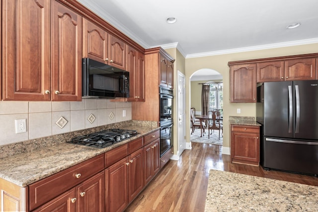 9732 Turnbridge Ct, Brentwood, TN 37027 - kitchen with black appliances, arched walkways, wood finished floors, light stone counters, and backsplash