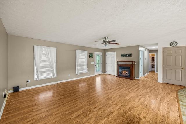 3135 Mullins Rd, Byrdstown, TN 38549 - unfurnished living room featuring a textured ceiling, light wood finished floors, a ceiling fan, and a glass covered fireplace