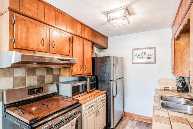 305 Bryant St, Watertown, TN 37184 - kitchen with appliances with stainless steel finishes, tile countertops, exhaust hood, light wood-type flooring, and tasteful backsplash