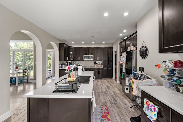 3723 Reed Rd, Indian Mound, TN 37079 - kitchen featuring stainless steel microwave, arched walkways, light wood finished floors, dark brown cabinetry, and a kitchen island with sink