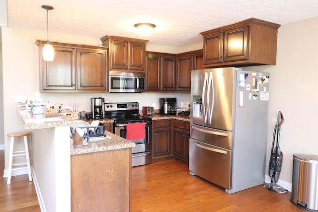 120 Mai Ridge Ln, Lafayette, TN 37083 - kitchen with appliances with stainless steel finishes, a peninsula, light wood-style flooring, hanging light fixtures, and a kitchen breakfast bar