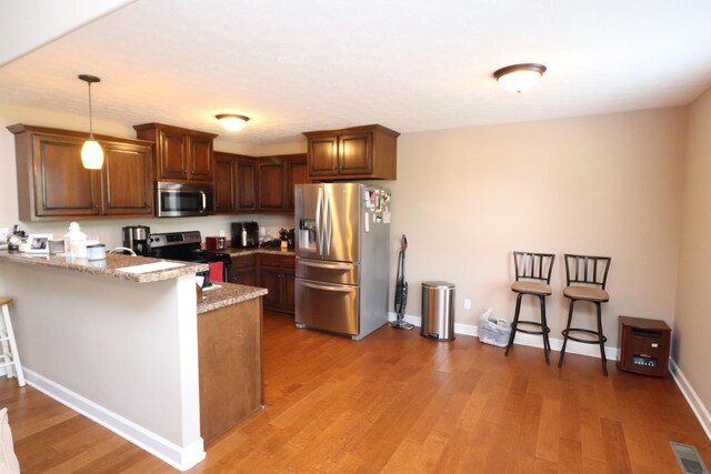 120 Mai Ridge Ln, Lafayette, TN 37083 - kitchen with appliances with stainless steel finishes, a peninsula, light wood-style floors, hanging light fixtures, and brown cabinetry