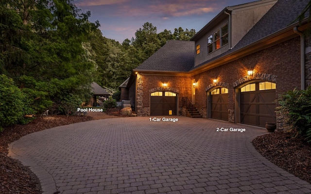 11 Saint Nicholas Way, Signal Mountain, TN 37377 - property exterior at dusk with curved driveway, a garage, brick siding, stone siding, and roof with shingles