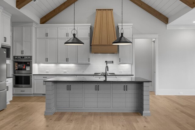 343 Circuit Rd, Franklin, TN 37064 - kitchen featuring appliances with stainless steel finishes, light wood-style floors, tasteful backsplash, dark stone counters, and a kitchen island with sink