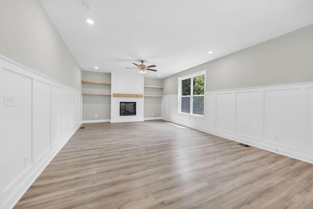 582 Pongracz Way, Clarksville, TN 37042 - unfurnished living room with a decorative wall, ceiling fan, light wood-style floors, a large fireplace, and wainscoting