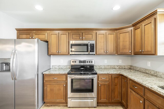 2075 Downstream Dr, Ashland City, TN 37015 - kitchen featuring appliances with stainless steel finishes, brown cabinets, light stone countertops, and recessed lighting