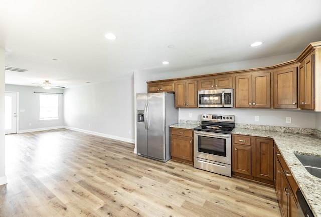 2075 Downstream Dr, Ashland City, TN 37015 - kitchen with appliances with stainless steel finishes, brown cabinets, light wood-type flooring, open floor plan, and light stone counters