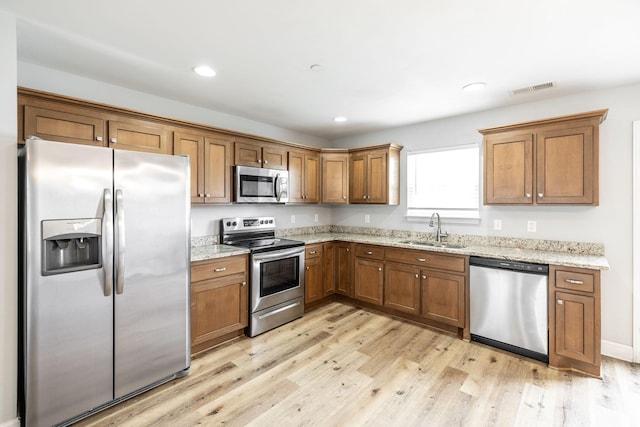 2075 Downstream Dr, Ashland City, TN 37015 - kitchen featuring appliances with stainless steel finishes, brown cabinetry, light wood-style flooring, light stone countertops, and recessed lighting