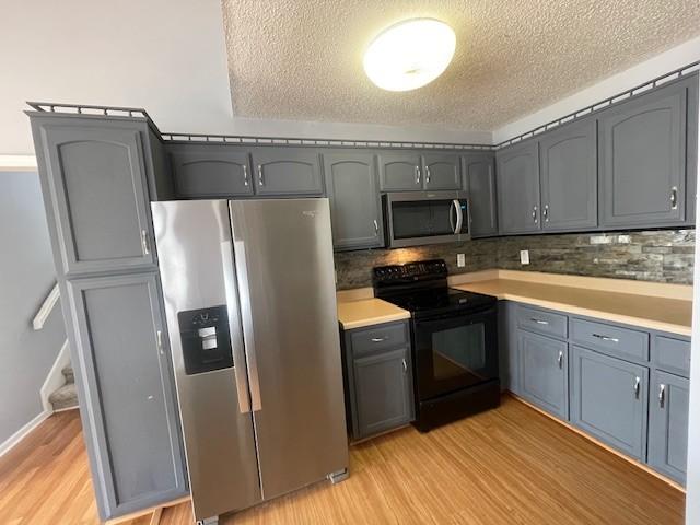 2750 Shepherds Ct, Woodlawn, TN 37191 - kitchen with appliances with stainless steel finishes, light wood-style flooring, a textured ceiling, backsplash, and gray cabinets