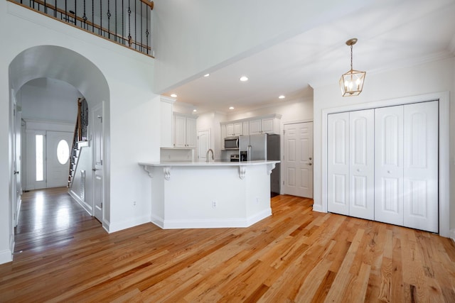 8539 Lexie Ln, Ooltewah, TN 37363 - kitchen featuring appliances with stainless steel finishes, a peninsula, a kitchen bar, light wood-style flooring, and ornamental molding
