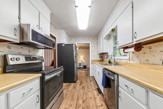 1150 Mattox Town Rd, Lawrenceburg, TN 38464 - kitchen with appliances with stainless steel finishes, wallpapered walls, white cabinetry, light countertops, and light wood finished floors