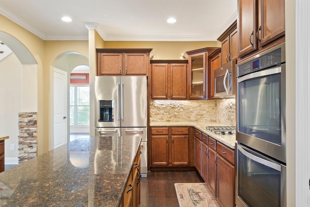 5010 Moretto Ct, Spring Hill, TN 37174 - kitchen featuring stainless steel appliances, brown cabinets, arched walkways, dark wood-type flooring, and glass insert cabinets