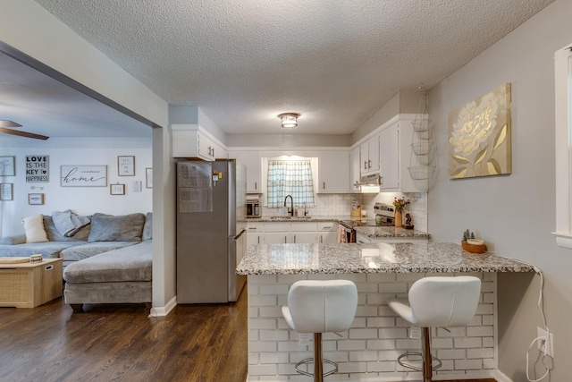 528 Maple St, Pulaski, TN 38478 - kitchen with appliances with stainless steel finishes, a peninsula, light stone counters, white cabinetry, and a textured ceiling