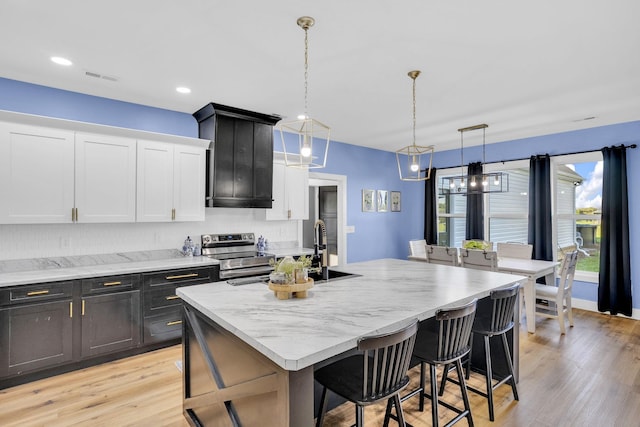 426 Maple Bend Rd, Winchester, TN 37398 - kitchen featuring stainless steel range with electric cooktop, an island with sink, white cabinets, a kitchen breakfast bar, and light wood-style flooring