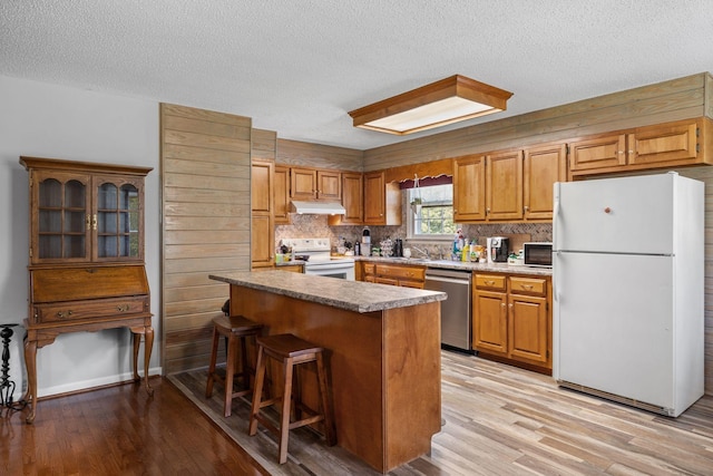 4628 Dugger Rd, Culleoka, TN 38451 - kitchen with white appliances, under cabinet range hood, light wood-style flooring, a textured ceiling, and a breakfast bar area
