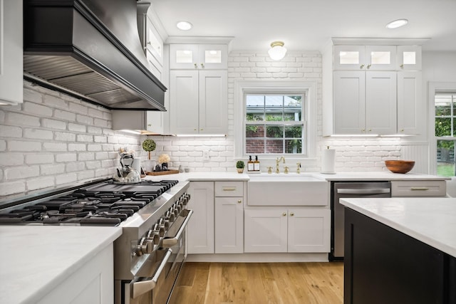 2641 Buckner Rd, Thompsons Station, TN 37179 - kitchen featuring appliances with stainless steel finishes, custom exhaust hood, light countertops, light wood-style flooring, and white cabinetry