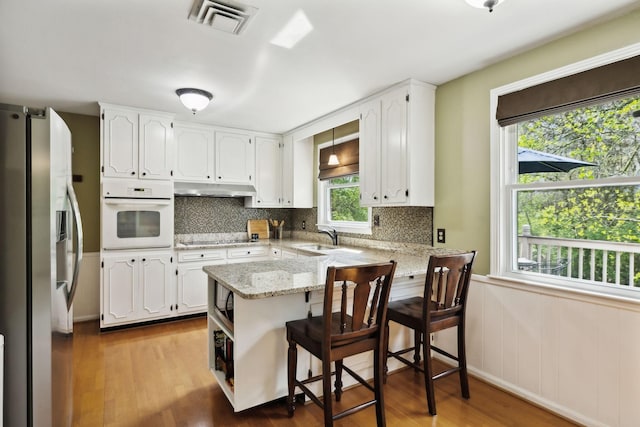 6002 Temple Rd, Nashville, TN 37221 - kitchen featuring oven, stainless steel refrigerator with ice dispenser, a peninsula, under cabinet range hood, and white cabinetry