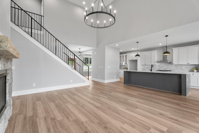 6021 Riverview Dr, Pegram, TN 37143 - unfurnished living room with stairway, light wood-style floors, a stone fireplace, a towering ceiling, and a chandelier