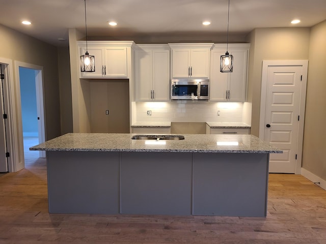 4211 Woods St, Old Hickory, TN 37138 - kitchen with stainless steel microwave, white cabinetry, decorative light fixtures, light stone counters, and a center island with sink