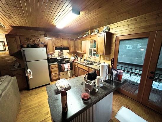 2933 Vanzant Bend Rd, Belvidere, TN 37306 - kitchen with stainless steel electric range, freestanding refrigerator, under cabinet range hood, wooden walls, and light wood-style floors