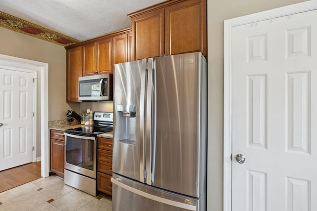 131 E Robertson Rd, Castalian Springs, TN 37031 - kitchen with stainless steel appliances, brown cabinetry, light tile patterned floors, light stone countertops, and a textured ceiling