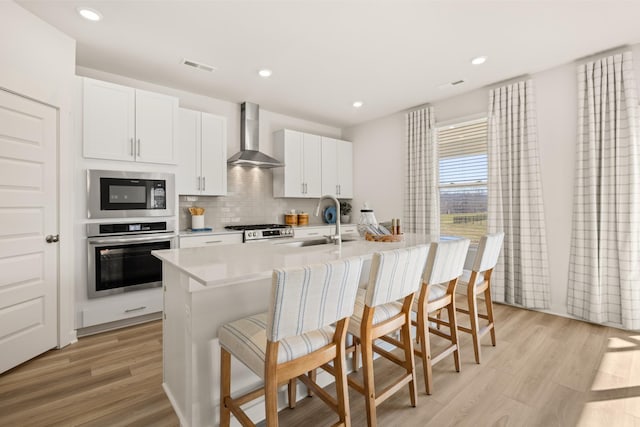 1243 Tucker Dr, Lebanon, TN 37087 - kitchen with appliances with stainless steel finishes, wall chimney exhaust hood, an island with sink, light wood-type flooring, and a breakfast bar area