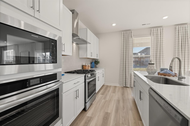 1243 Tucker Dr, Lebanon, TN 37087 - kitchen featuring appliances with stainless steel finishes, wall chimney exhaust hood, light wood finished floors, white cabinets, and decorative backsplash