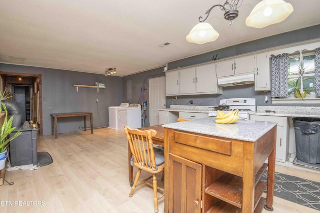 197 Wedgewood Ln, Spring City, TN 37381 - kitchen with white gas stove, washing machine and clothes dryer, under cabinet range hood, light wood finished floors, and a wood stove