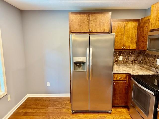 208 Broadrick St, Tullahoma, TN 37388 - kitchen with appliances with stainless steel finishes, light wood-style floors, tasteful backsplash, and brown cabinets