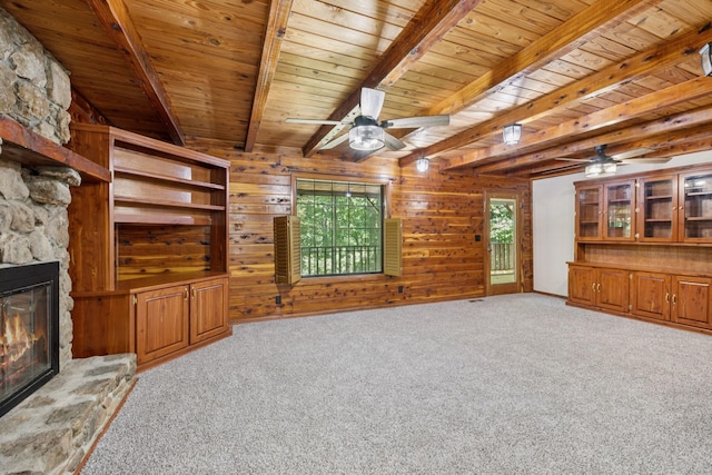 584 Mccord Hollow Rd, Hohenwald, TN 38462 - unfurnished living room featuring a ceiling fan, a wood ceiling with exposed beams, a stone fireplace, light colored carpet, and wood walls