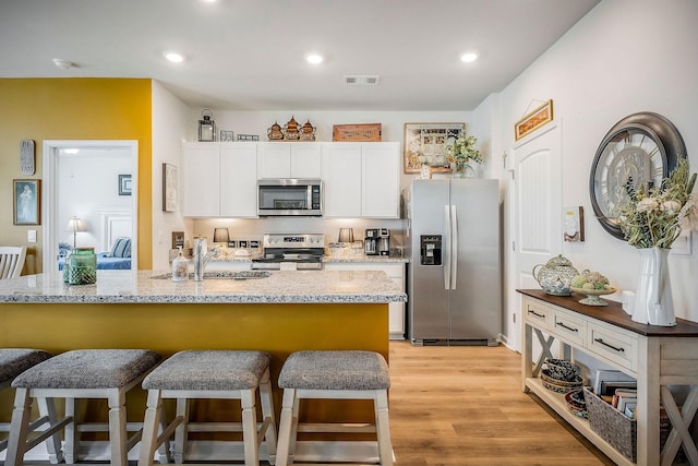 155 Nunally Dr, Baxter, TN 38544 - kitchen with appliances with stainless steel finishes, a breakfast bar, white cabinets, light wood-style flooring, and recessed lighting