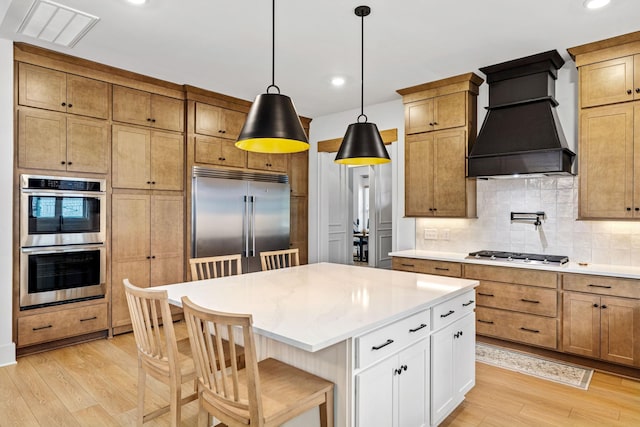 5831 Branta Dr, Franklin, TN 37064 - kitchen with stainless steel appliances, custom range hood, light wood finished floors, backsplash, and hanging light fixtures
