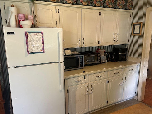 217 Millcreek Dr, Loretto, TN 38469 - kitchen with freestanding refrigerator, stainless steel microwave, light countertops, white cabinets, and wallpapered walls