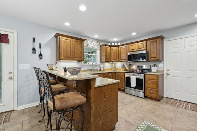 1550 Beech Bottom Rd, Watertown, TN 37184 - kitchen featuring appliances with stainless steel finishes, a peninsula, brown cabinets, a breakfast bar, and light stone counters